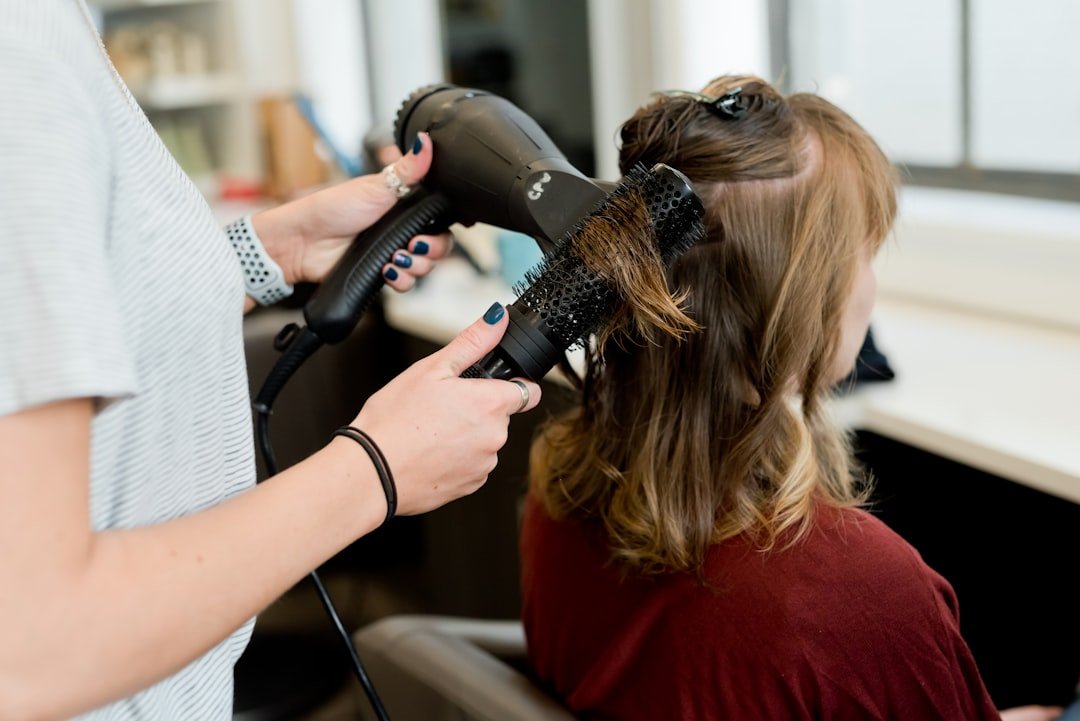 A woman applying a heat protectant spray to her hair before using a styling tool, surrounded by hair care products.