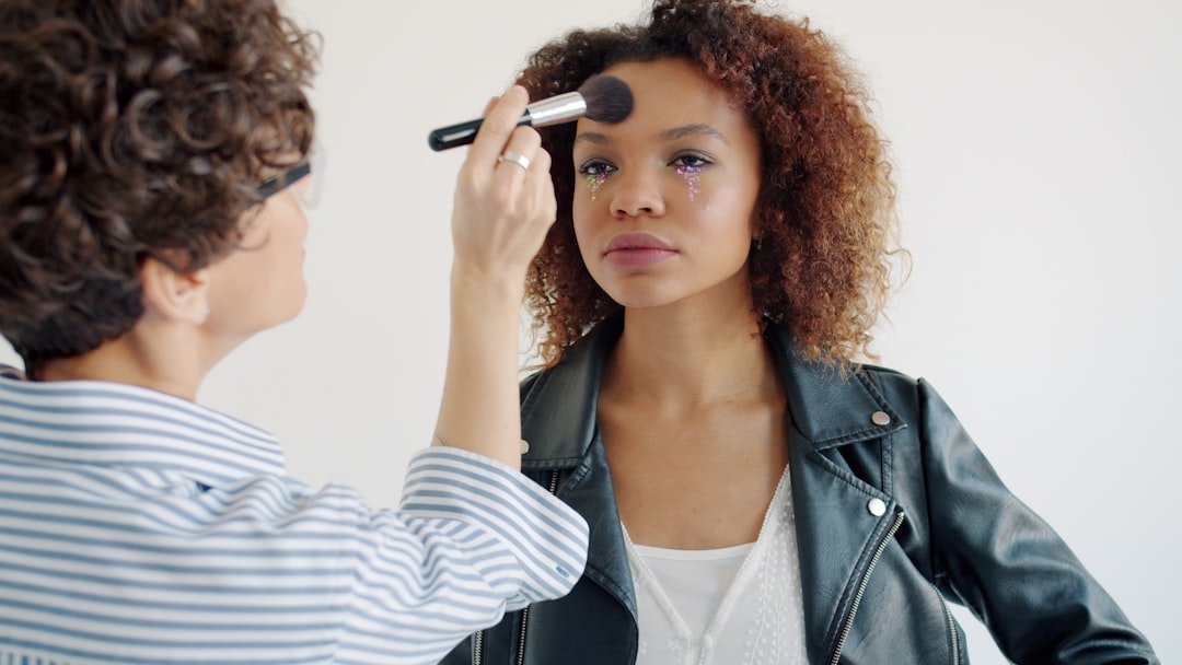 A makeup artist applies face makeup with a large brush to a woman's forehead.