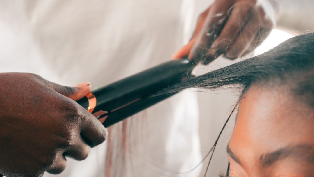 Close-up of a stylist using a flat iron and comb on a section of a person's hair.