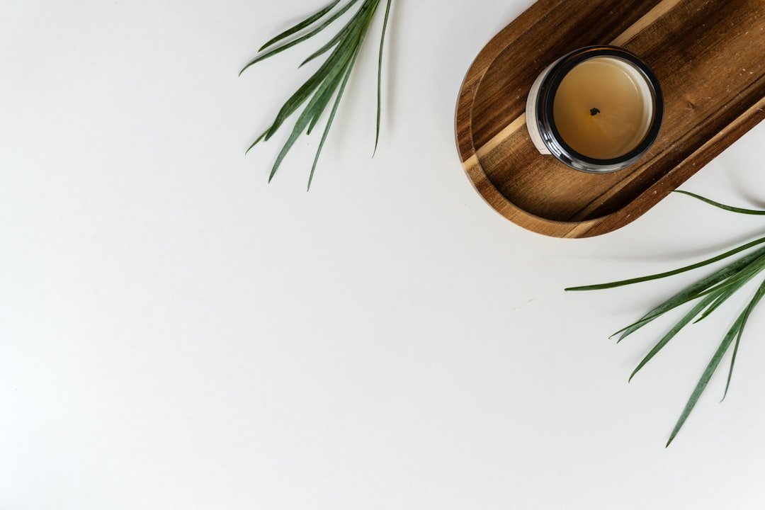 Overhead view of a candle in a wooden tray surrounded by green palm leaves on a clean white surface.