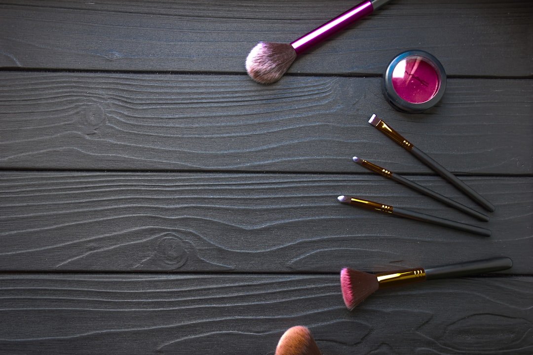 Several makeup brushes and a pot of pink cosmetic pigment arranged on a dark wooden surface.