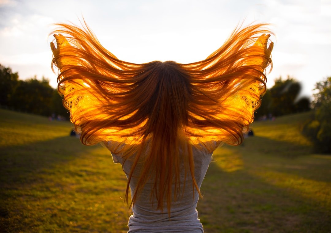Backlit view of a person outdoors lifting and spreading their long, flowing hair with both hands.
