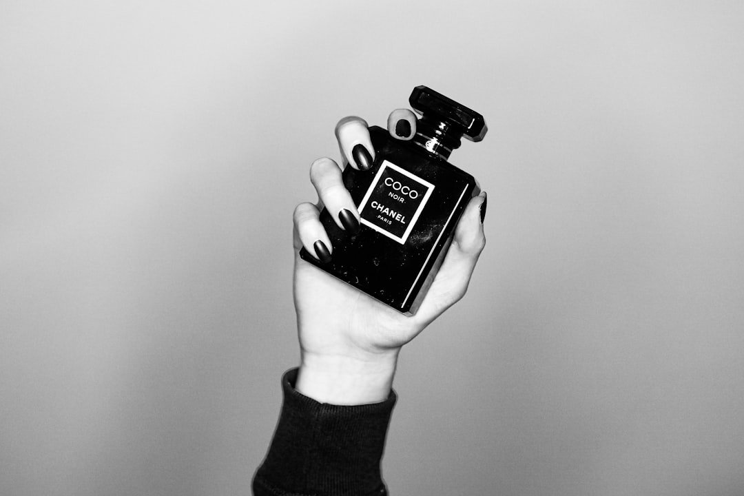 Black-and-white image of a manicured hand holding a luxury perfume bottle.