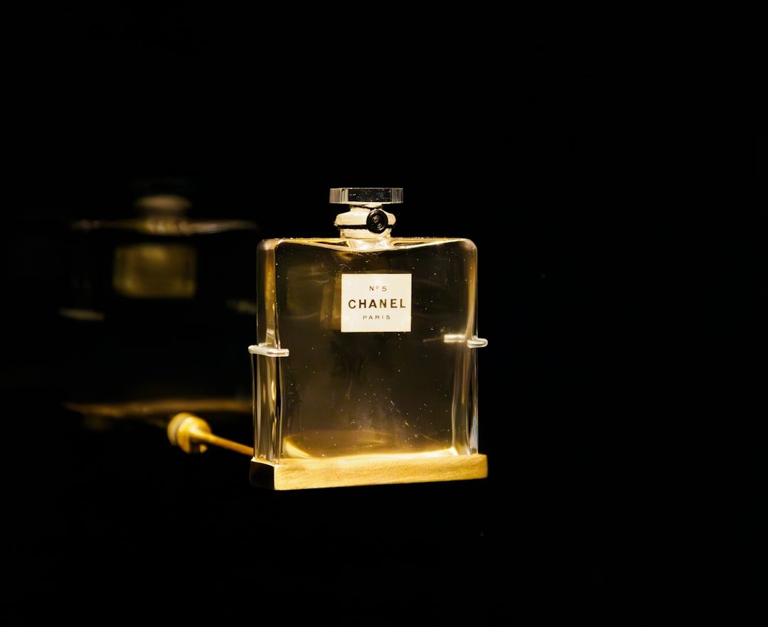 A glass perfume bottle containing amber liquid is displayed against a dark background.