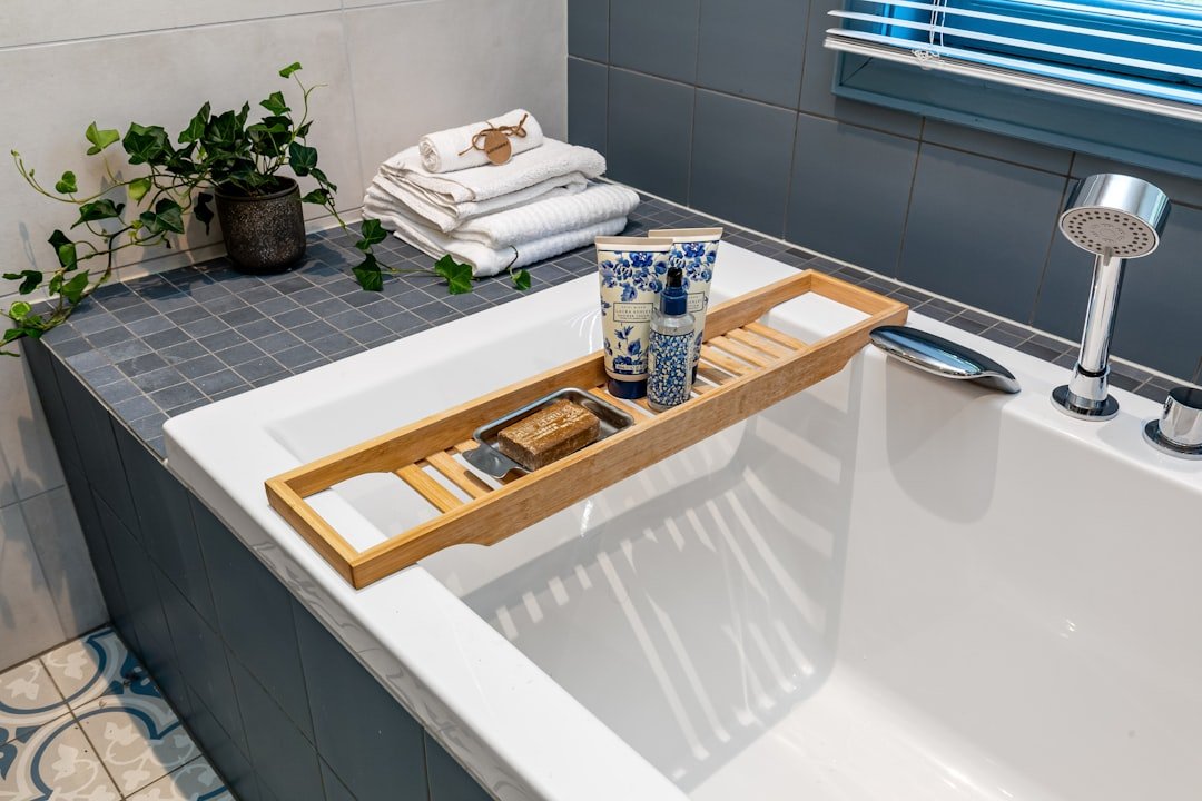 A clean bathtub styled with a wooden bath tray holding body-care products and soap, with folded towels and a trailing plant nearby.