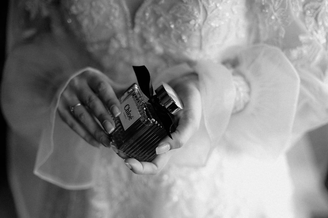 Black-and-white close-up of a person holding a luxury fragrance bottle.